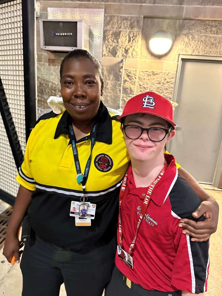 MetroLink rider Ryan wearing a St. Louis Cardinals hat and Cardinals Event Staff polo shirt posing with a Metro Transit Security Specialist